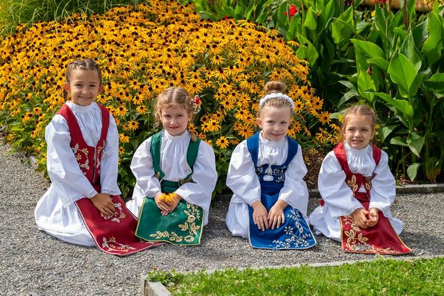 Vier Mädchen der Teslići in farbigen Trachten vor Blumen